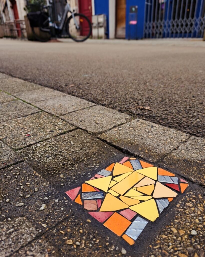 Mosaïque urbaine réalisée à Bayonne, Fresque collective à Emmaüs, Atelier participatif de mosaïque, fresque mosaïque urbaine Bayonne Elzarra, fresques en mosaïque, mosaïque urbaine, créations participatives, art public Pays Basque, Petites mosaïques urbaines réparant le bitume dans l’espace public, une démarche artistique engagée